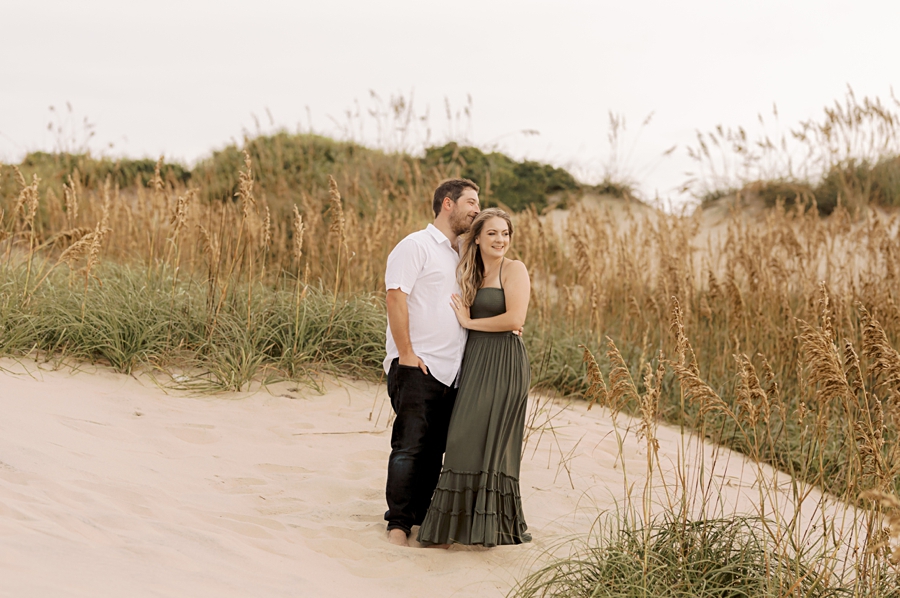 engaged couple cuddling on dunes in nags head, nc by sharon elizabeth co