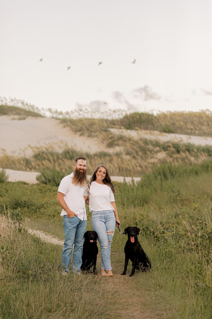 couple posing with dogs on dunes, sharon elizabeth co