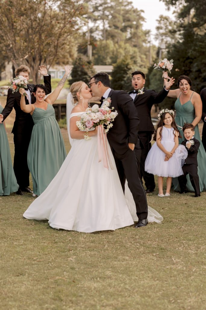 bride and groom kissing with wedding party cheering at duck woods country club by sharon elizabeth co