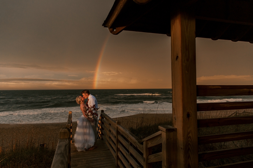 bride and groom hug on wooden pier at sunset on Kill Devil Hills beach