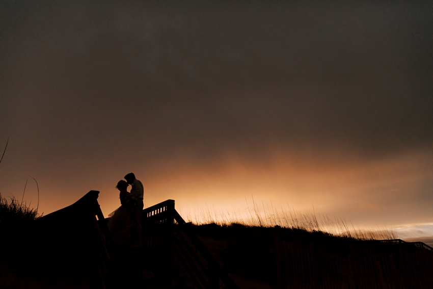 sunset portraits of bride and groom as silhouettes on top of ridge at beach