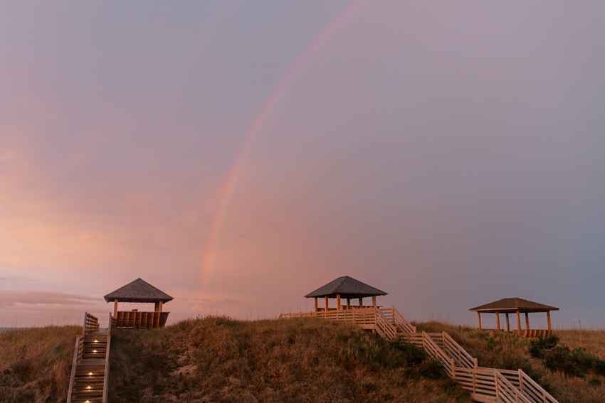 rainbow in purple sky between wooden beach gazebos at Kill Devil Hills