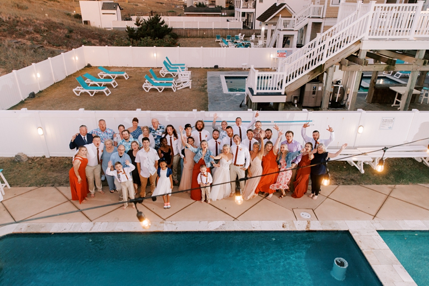 bride and groom pose with wedding party by pool at beach house in Kill Devil Hills