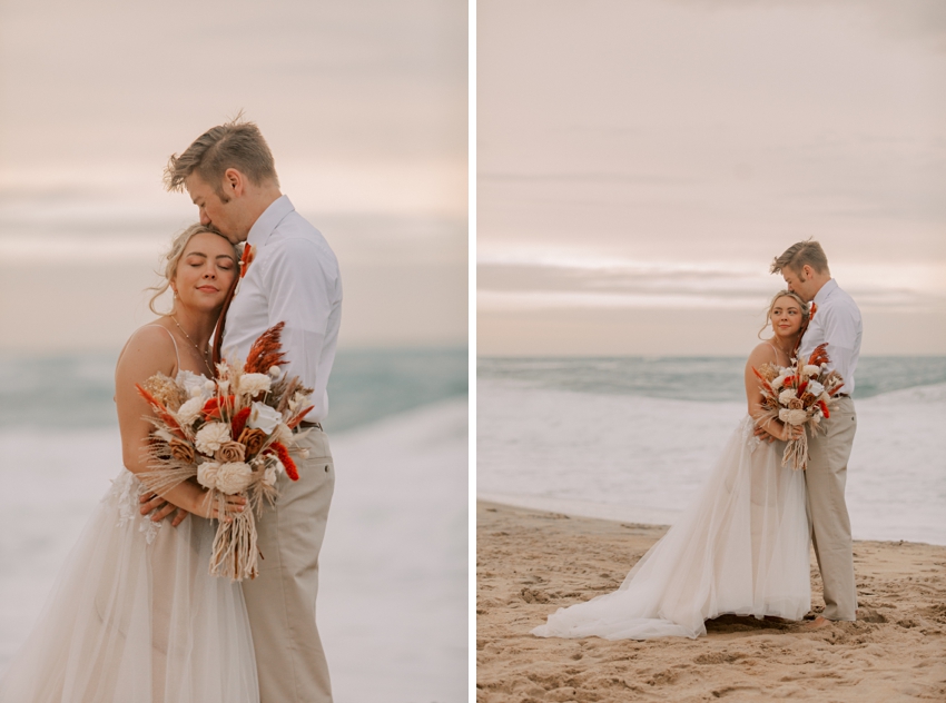 newlyweds hug at sunset in front of ocean on Kill Devil Hills beach