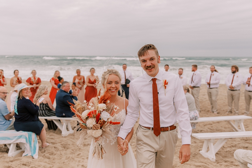 bride and groom laugh walking up aisle after beach ceremony in Kill Devil Hills