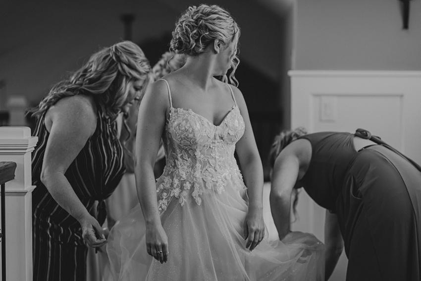 bridesmaids and mom help bride into wedding dress in beach house 