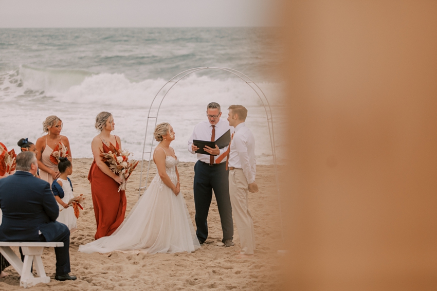 bride and groom hold hands during ceremony on beach in front of ocean