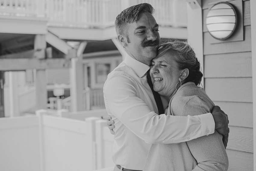 groom hugs mom next to him during photos at beach house 