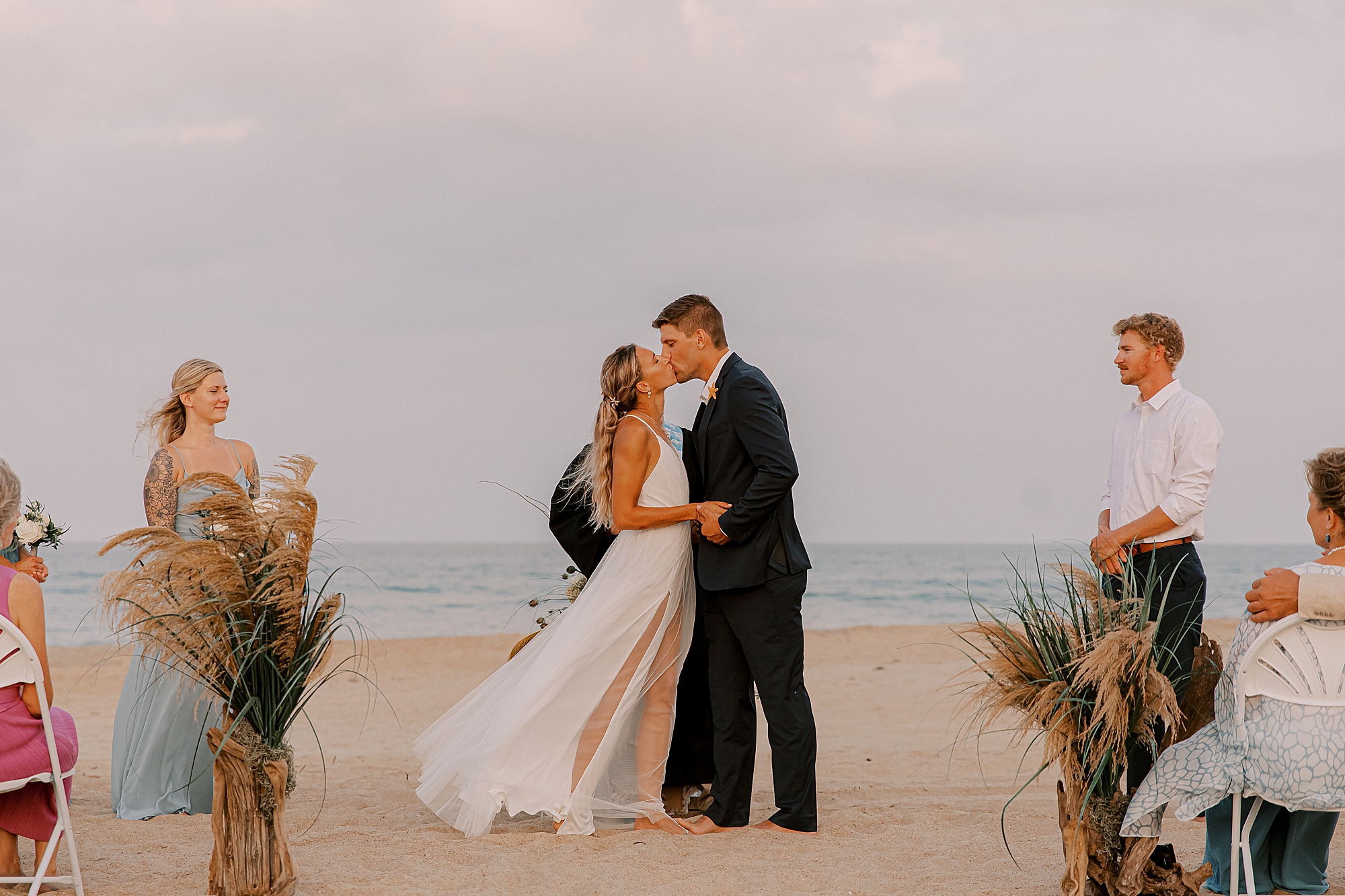 newlyweds kiss on the sand during private beach cottage wedding ceremony 