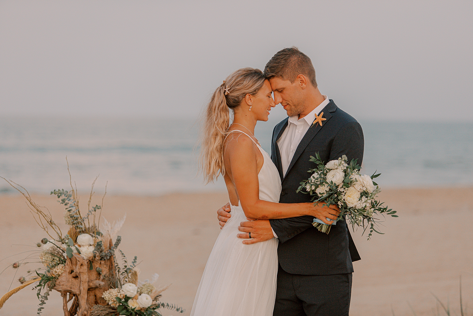 bride and groom hug touching foreheads on beach in Kill devil hills 