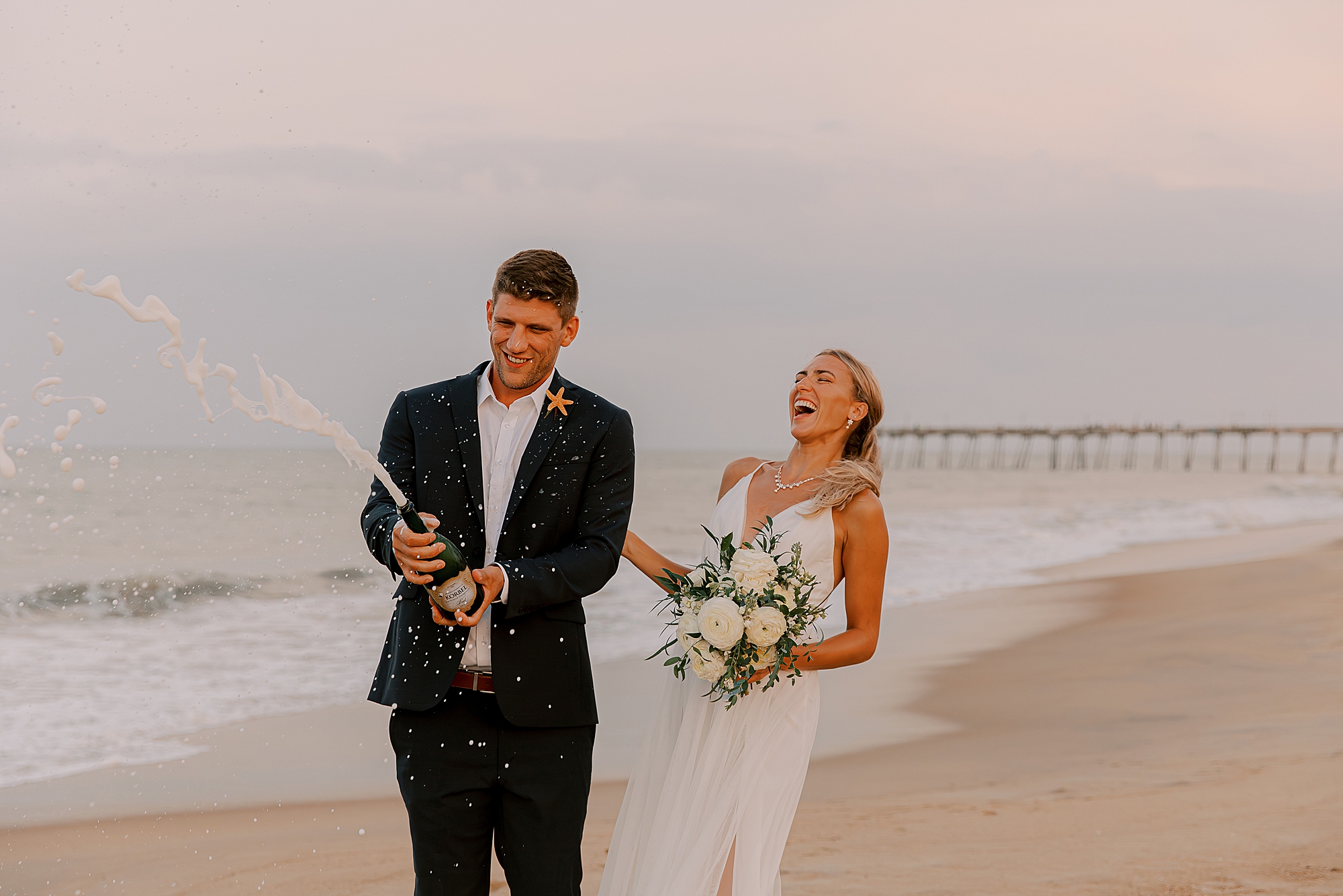 bride and groom pop champagne laughing on beach