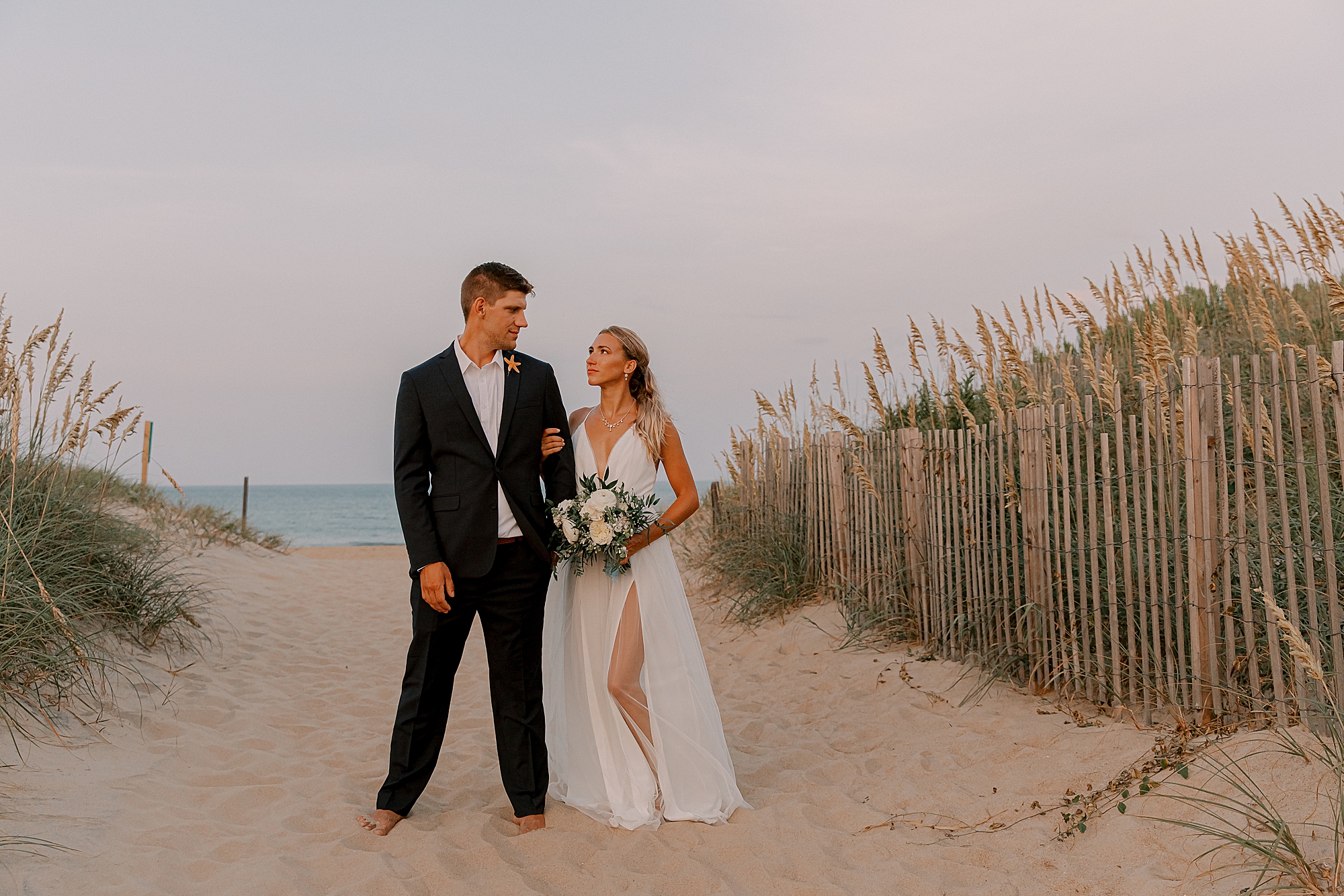 bride holds groom's arm looking up at him between sand dunes 