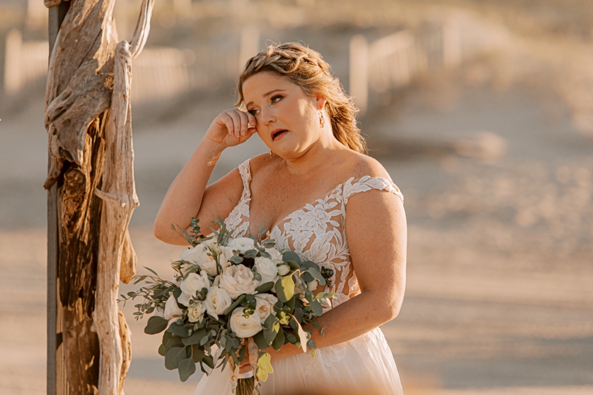 bride wipes away tear during wedding day ceremony on the beach 