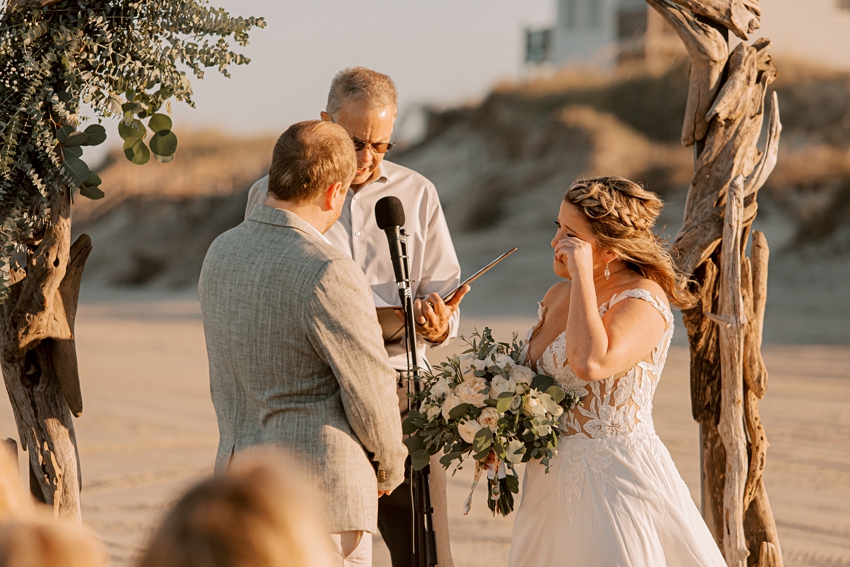 bride wipes away tear during wedding ceremony on beach