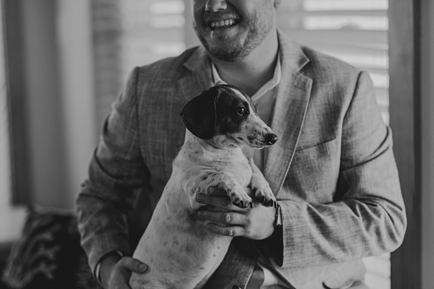 man holds small dog on his lap in beach house before wedding