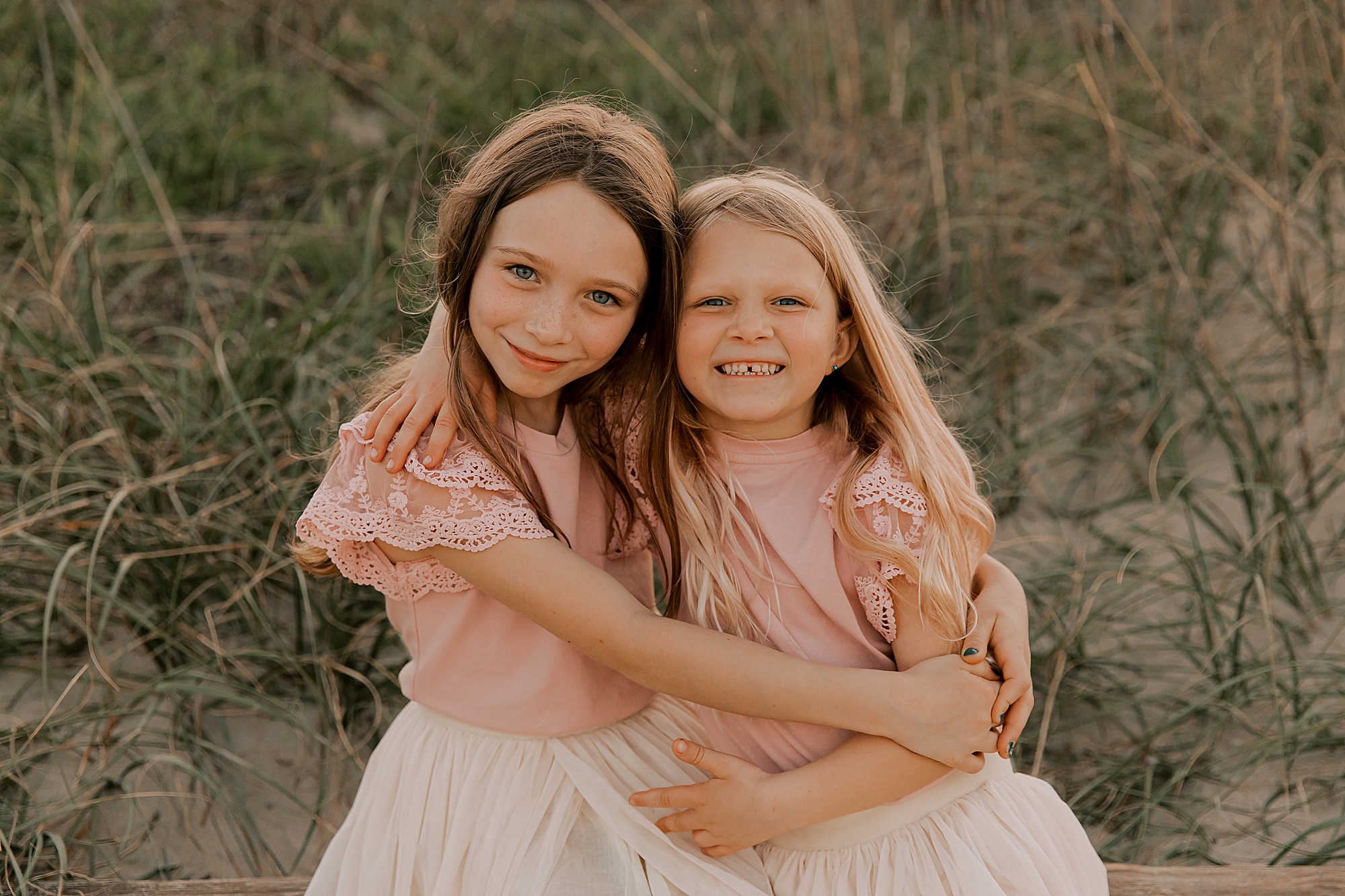 two sisters hug in pink and white outfits on nags head beach