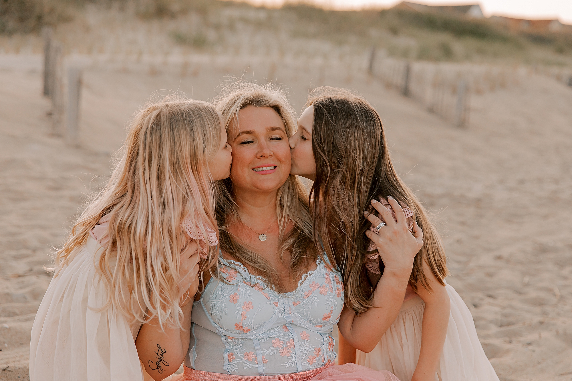 two girls kiss mom's cheek during mommy + me photos at nags head pier