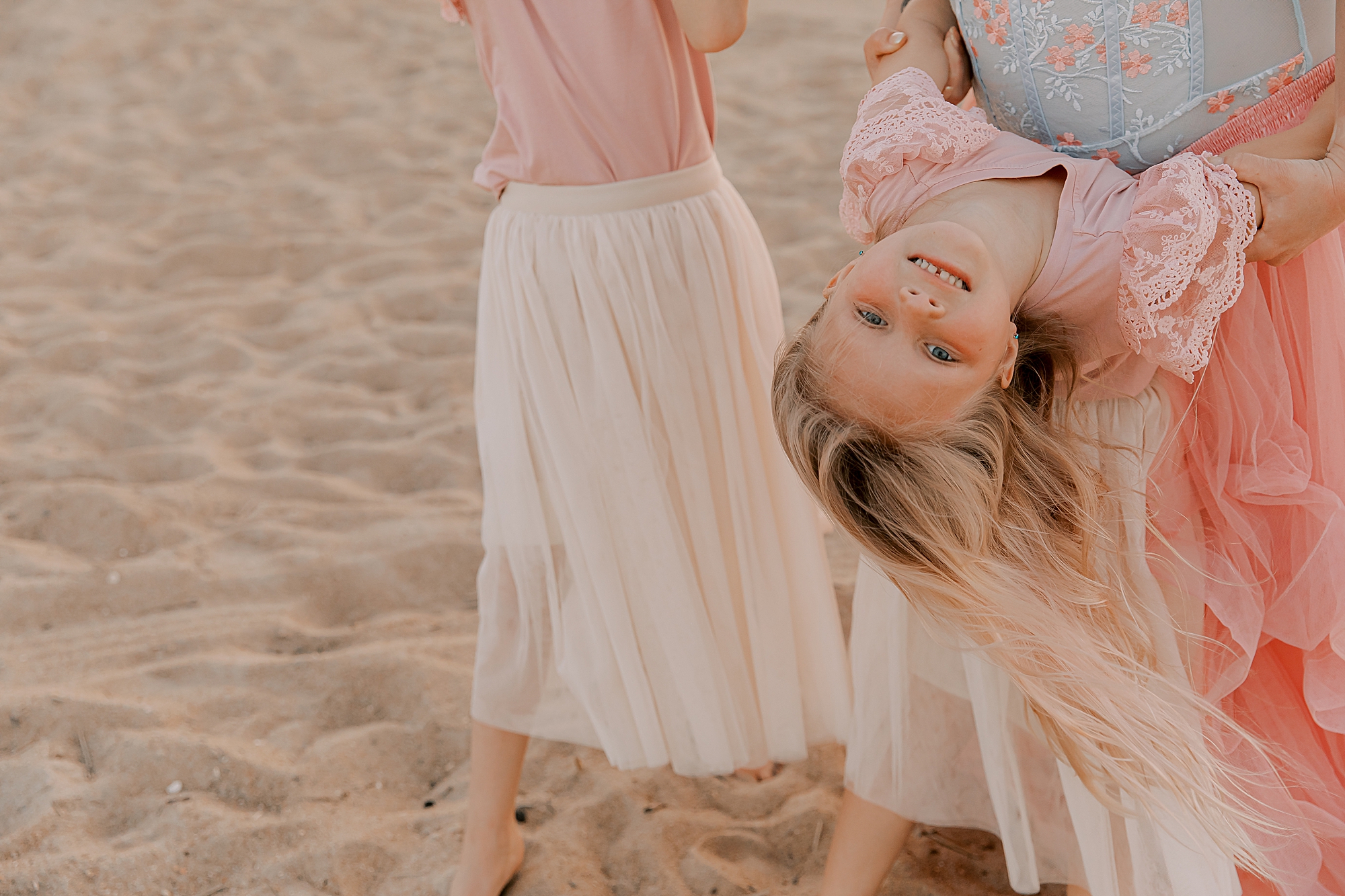 mom holds daughter upside down on the beach