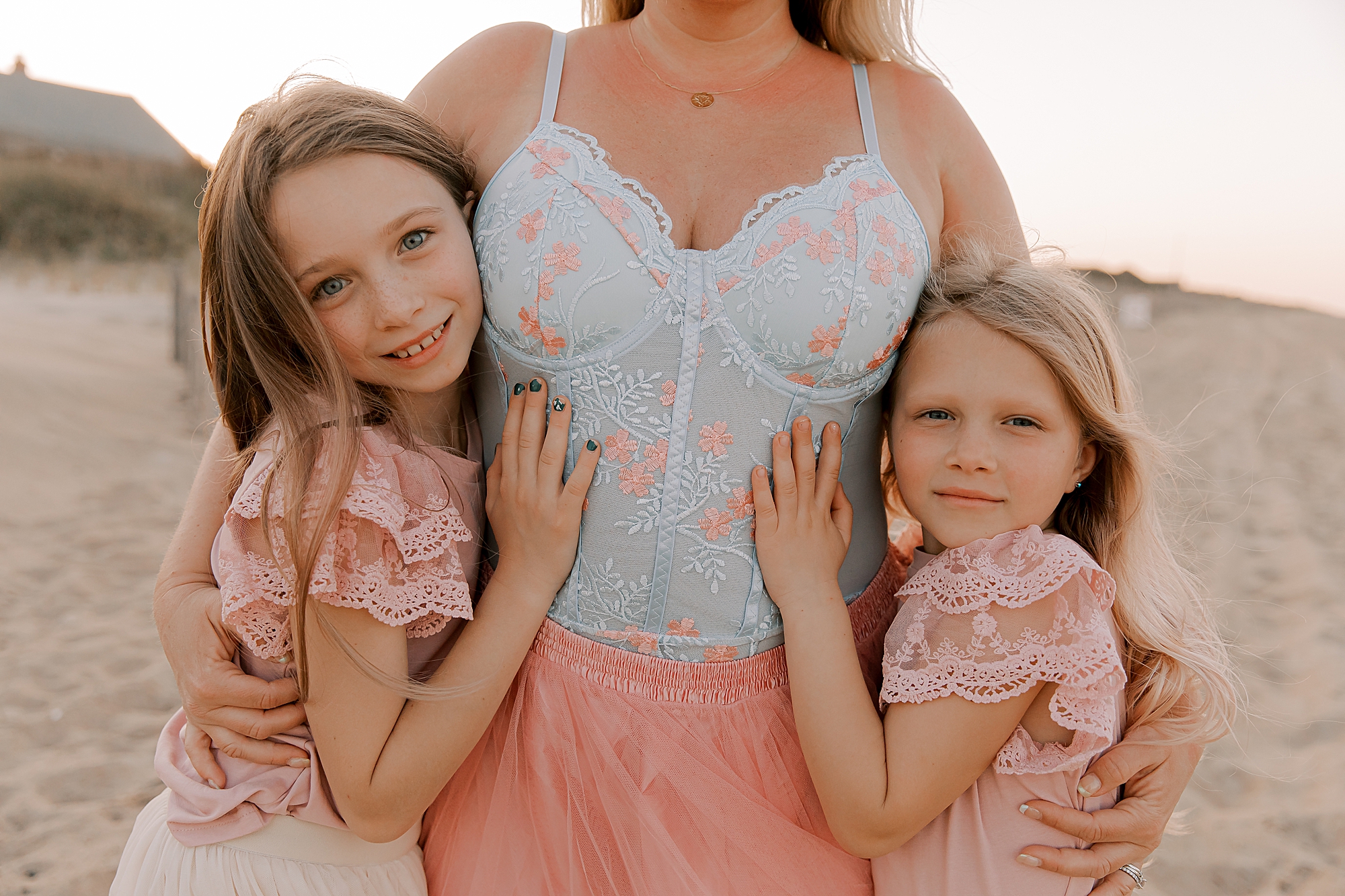 mom holds daughters to her hugging on the beach 