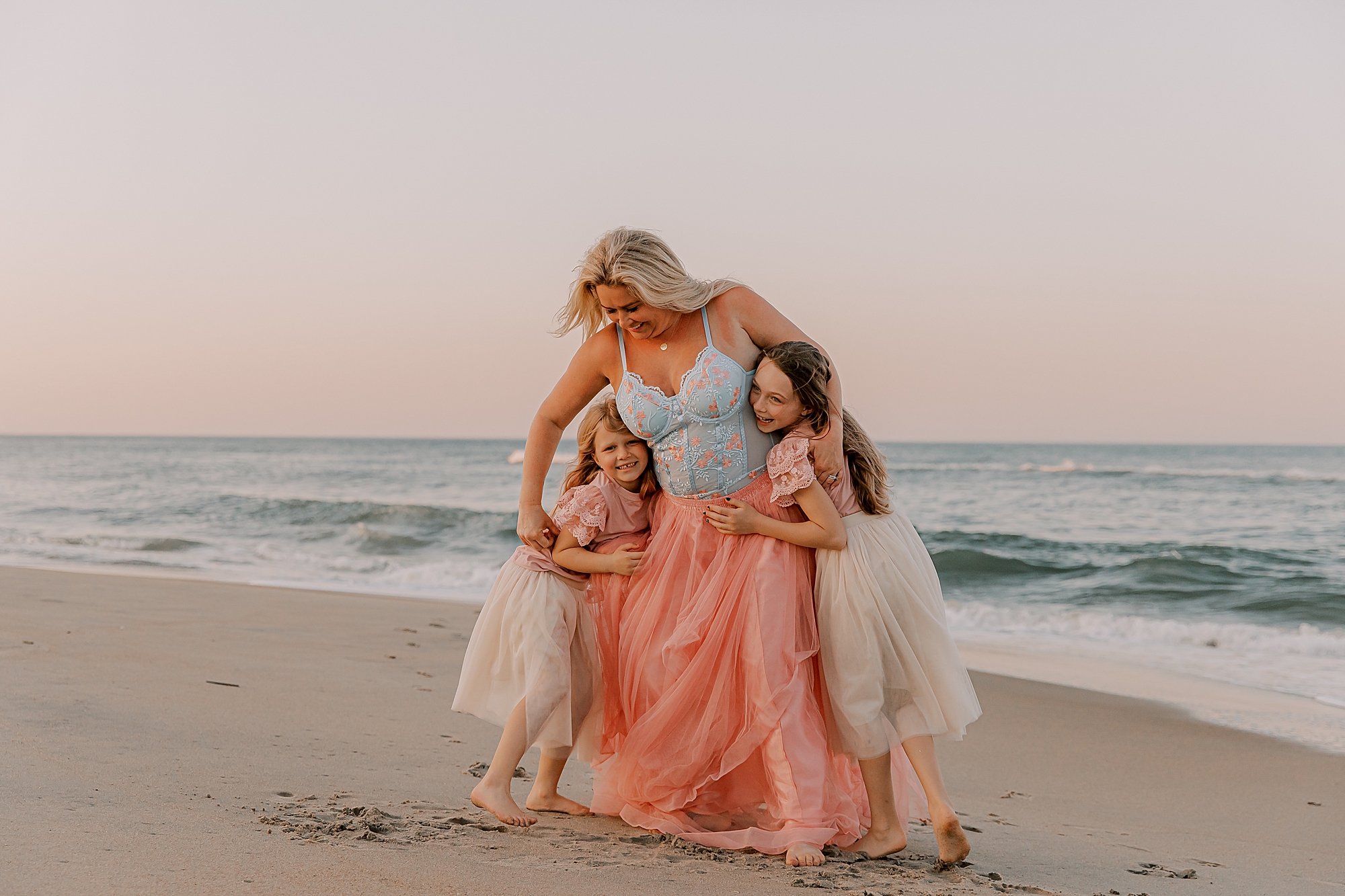 two daughters hug mom on the sand at sunset