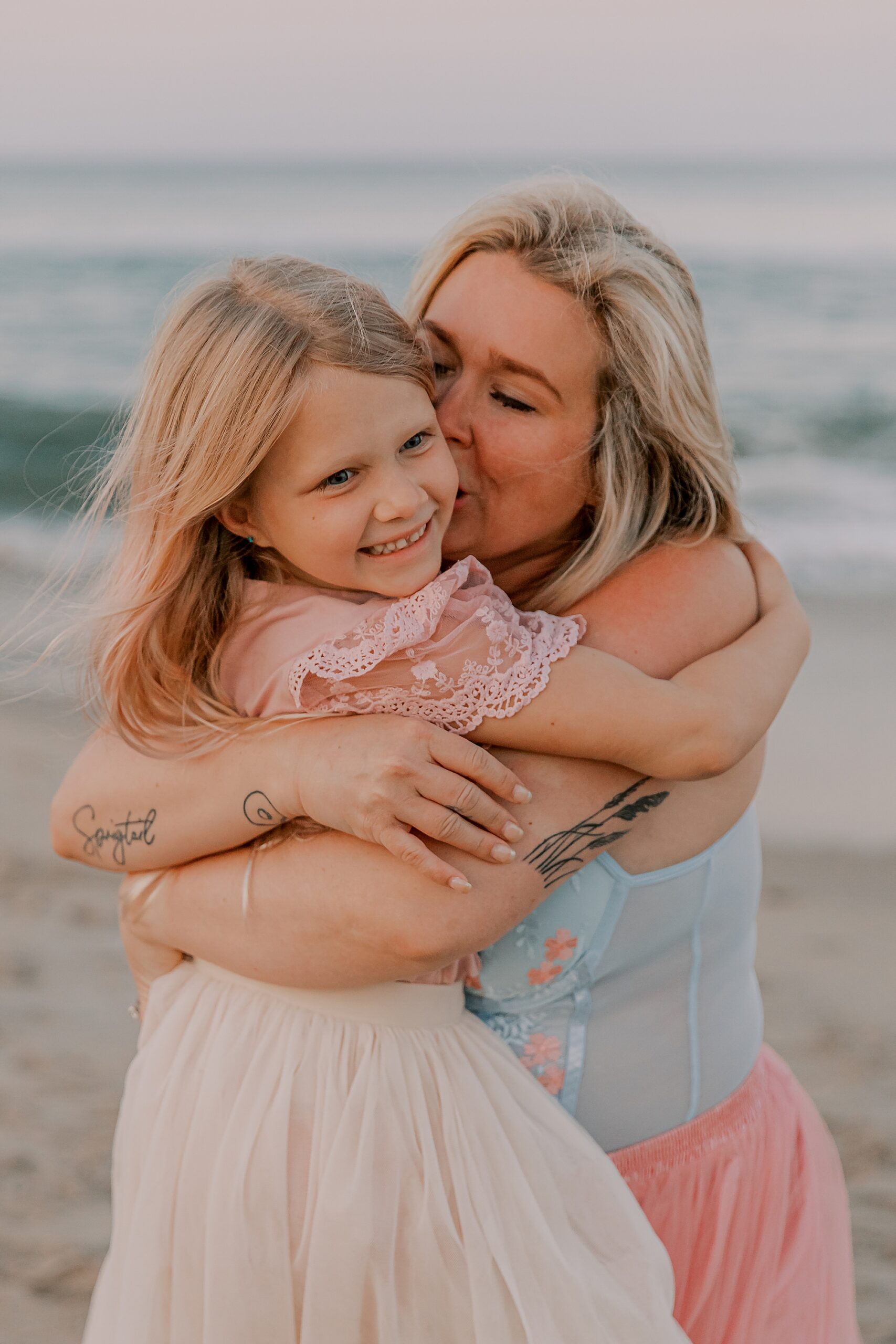 mom hugs daughter kissing her check during photos on nags head nc