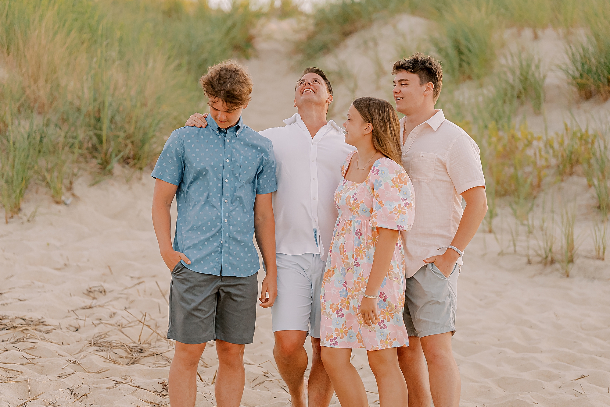 dad throws his head back laughing with three teenage kids during outer banks family photos