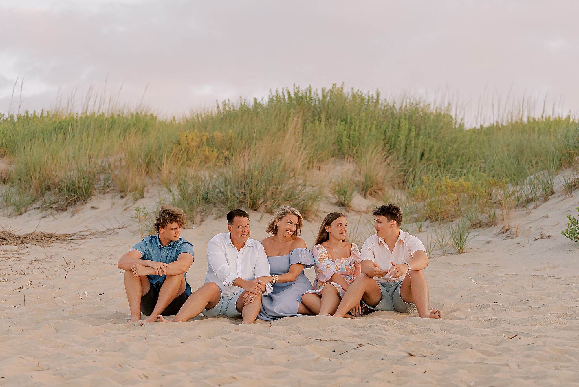 family of five sits in front of sand dunes during outer banks family photos