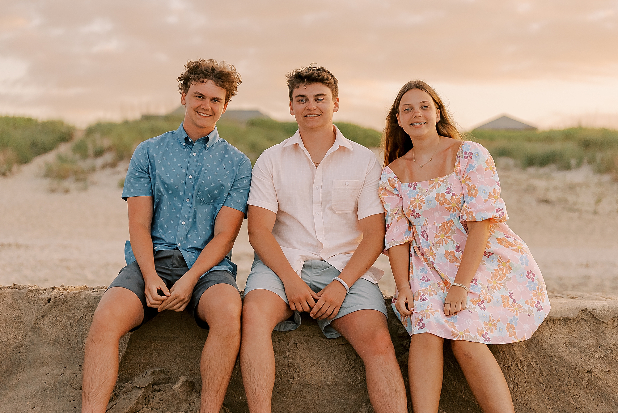 three teenagers sit on sand dune on edge of the beach