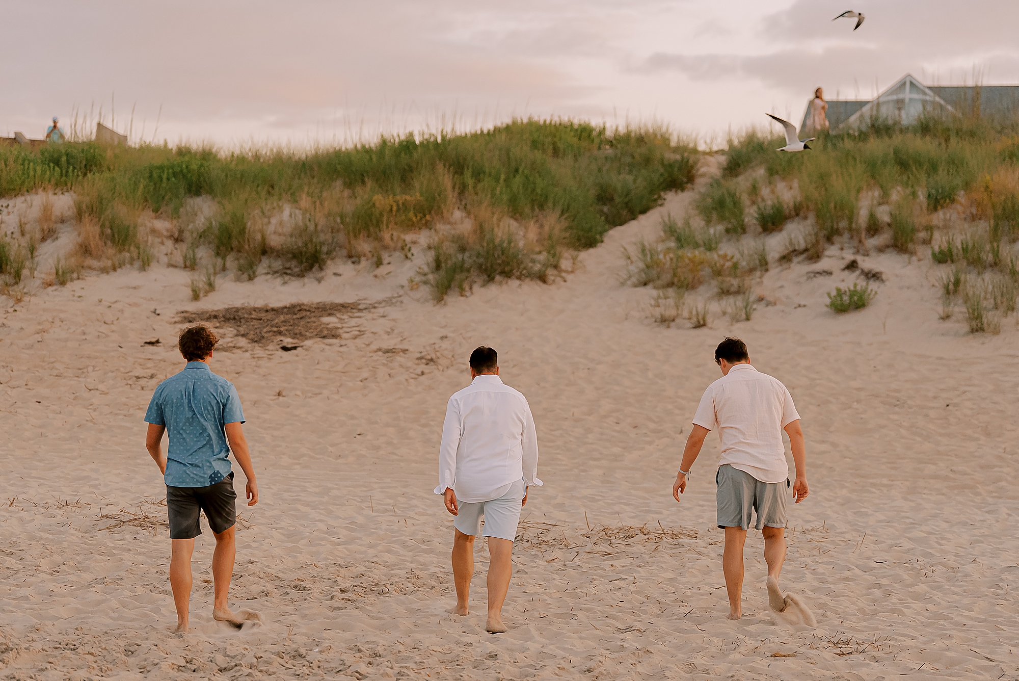 dad and two teenage sons walk towards sand dunes during outer banks family photos