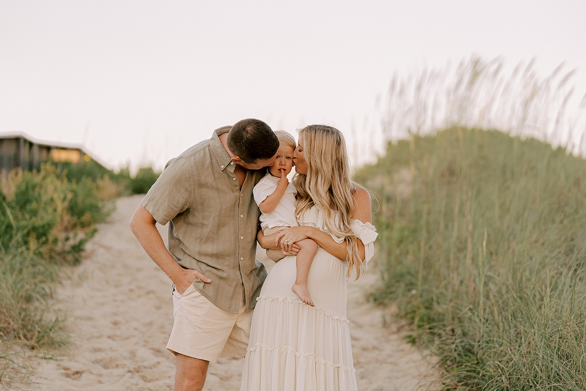 mom and dad lean to kiss toddler during family photos in the outer banks