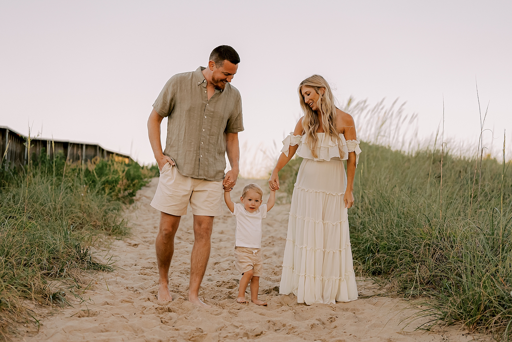 mom and dad hold toddler's hand walking down beach dune in the outer banks 