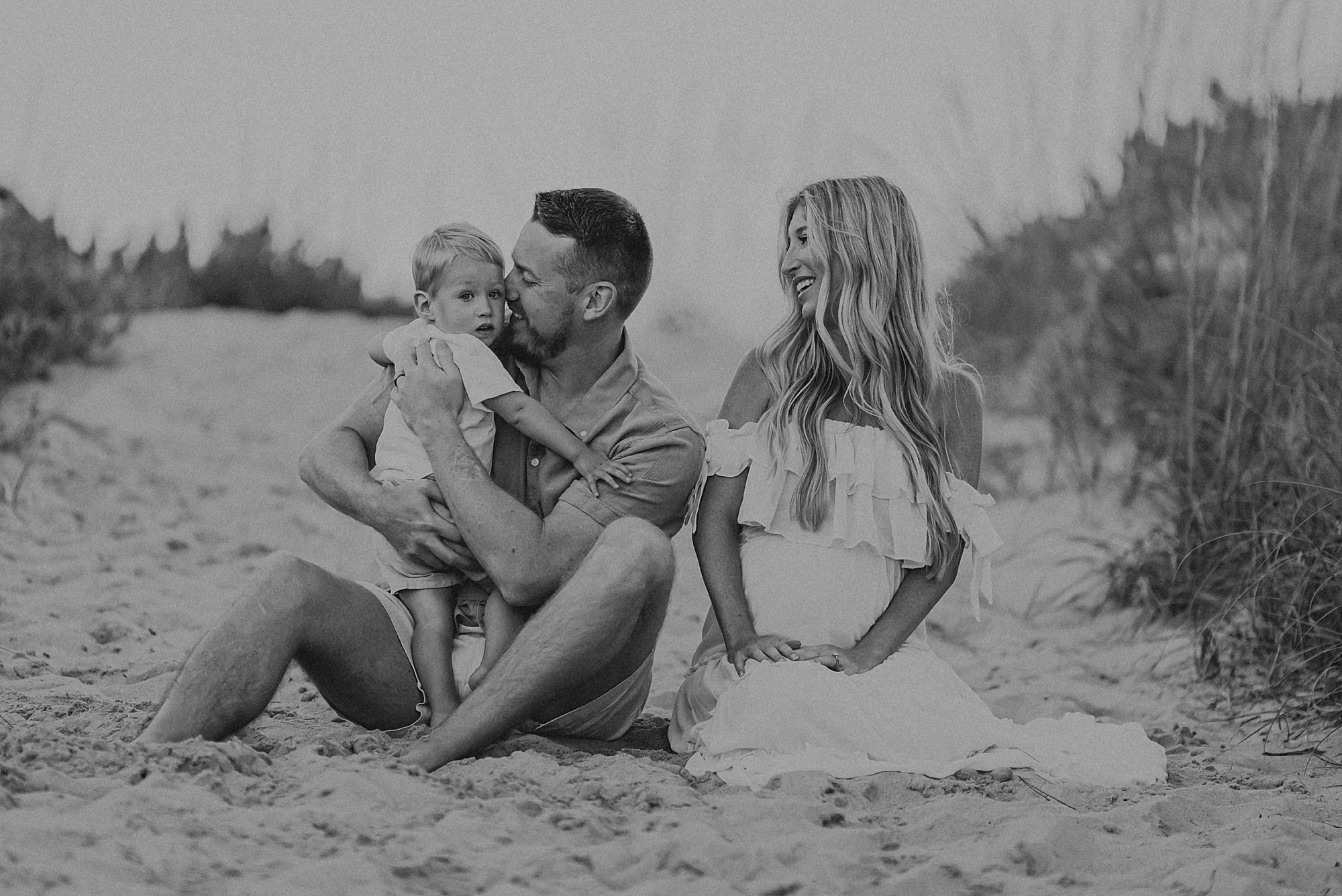 mom and dad snuggle with son during family photos on the beach 