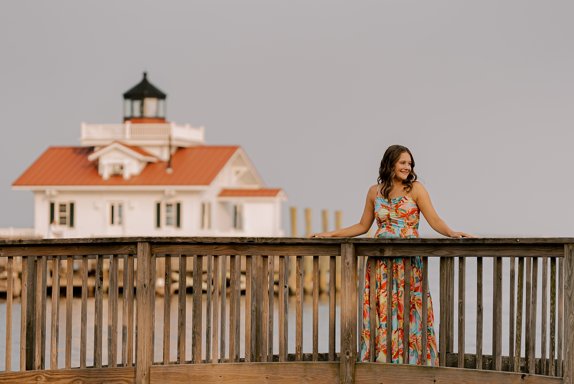 high school senior leans on wooden railing outside Manteo lighthouse 