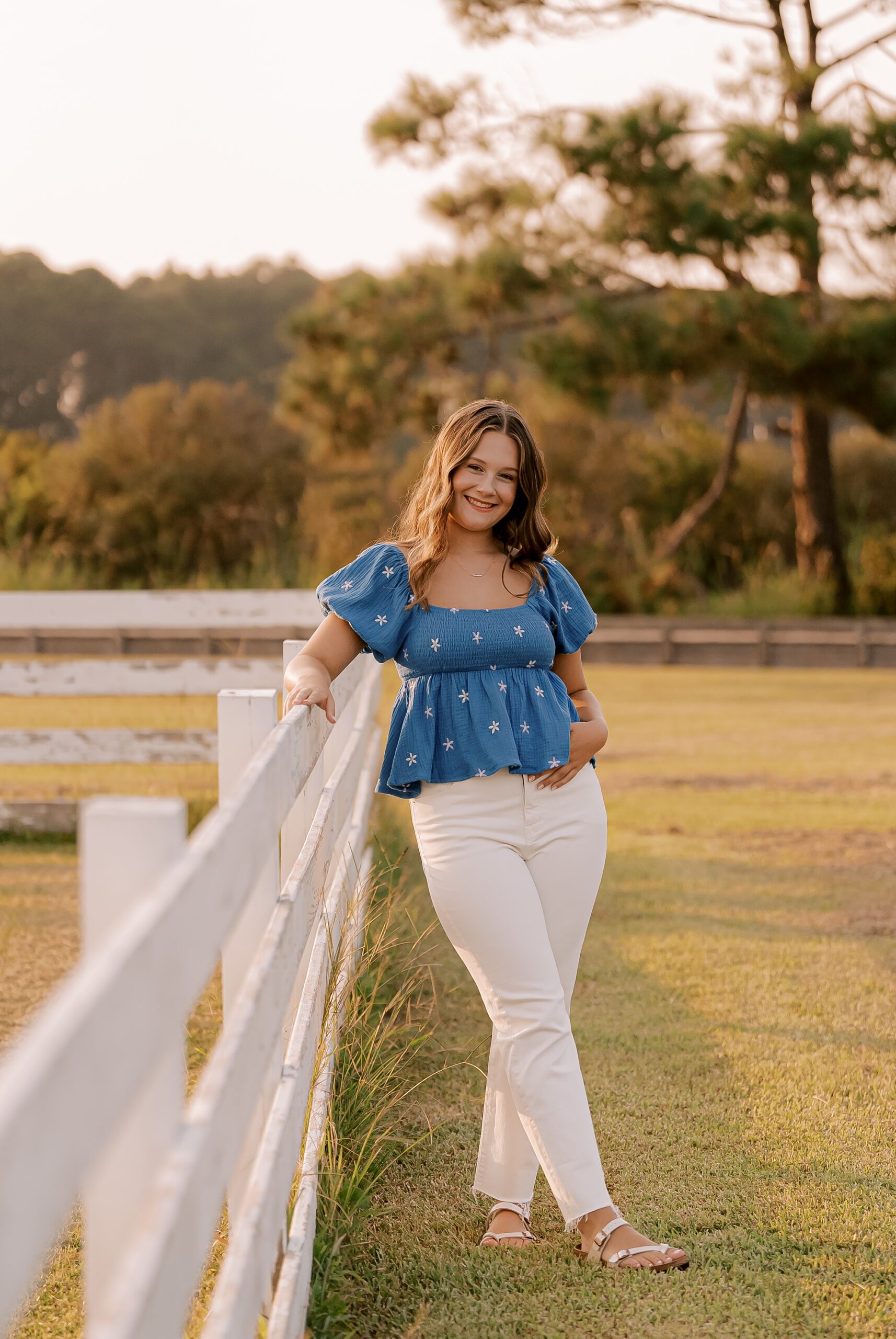 teenager girl leans on white fence during outer banks senior portraits