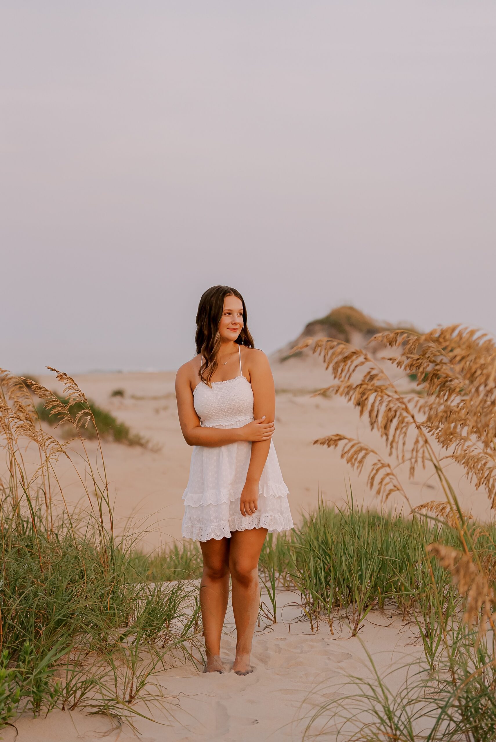 young woman in short white dress poses on sand dunes on the Oregon inlet