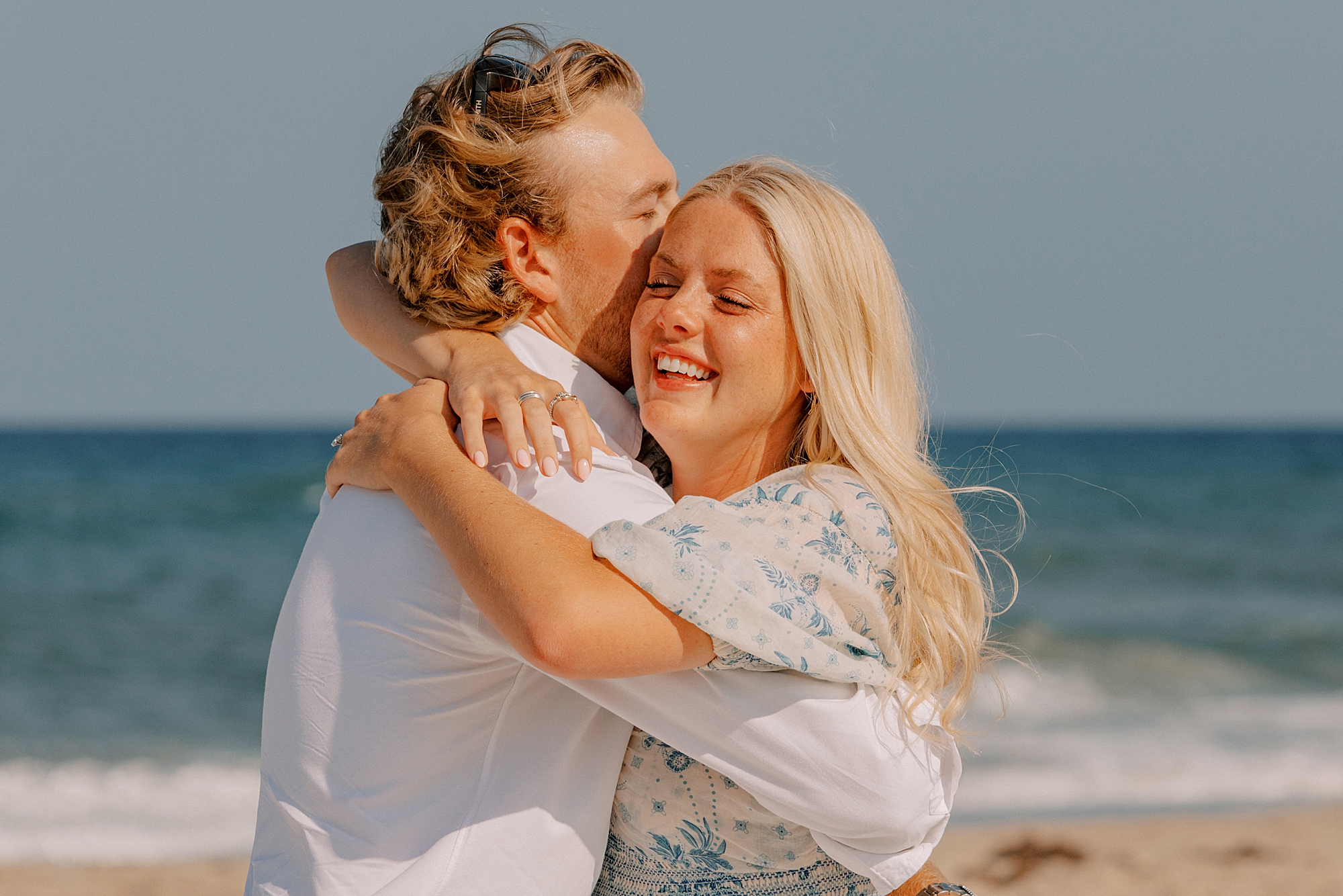 woman laughs hugging man after proposal on the beach