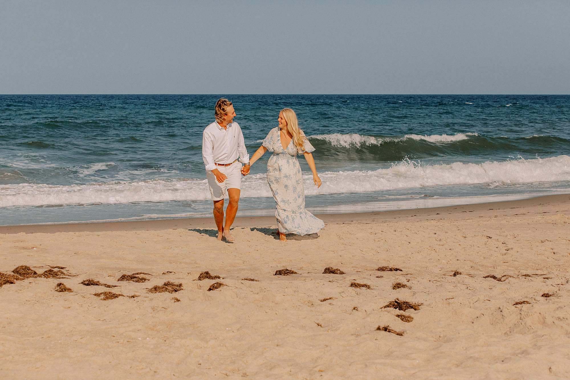 engaged couple holds hands walking on beach after proposal on the beach in kitty hawk 