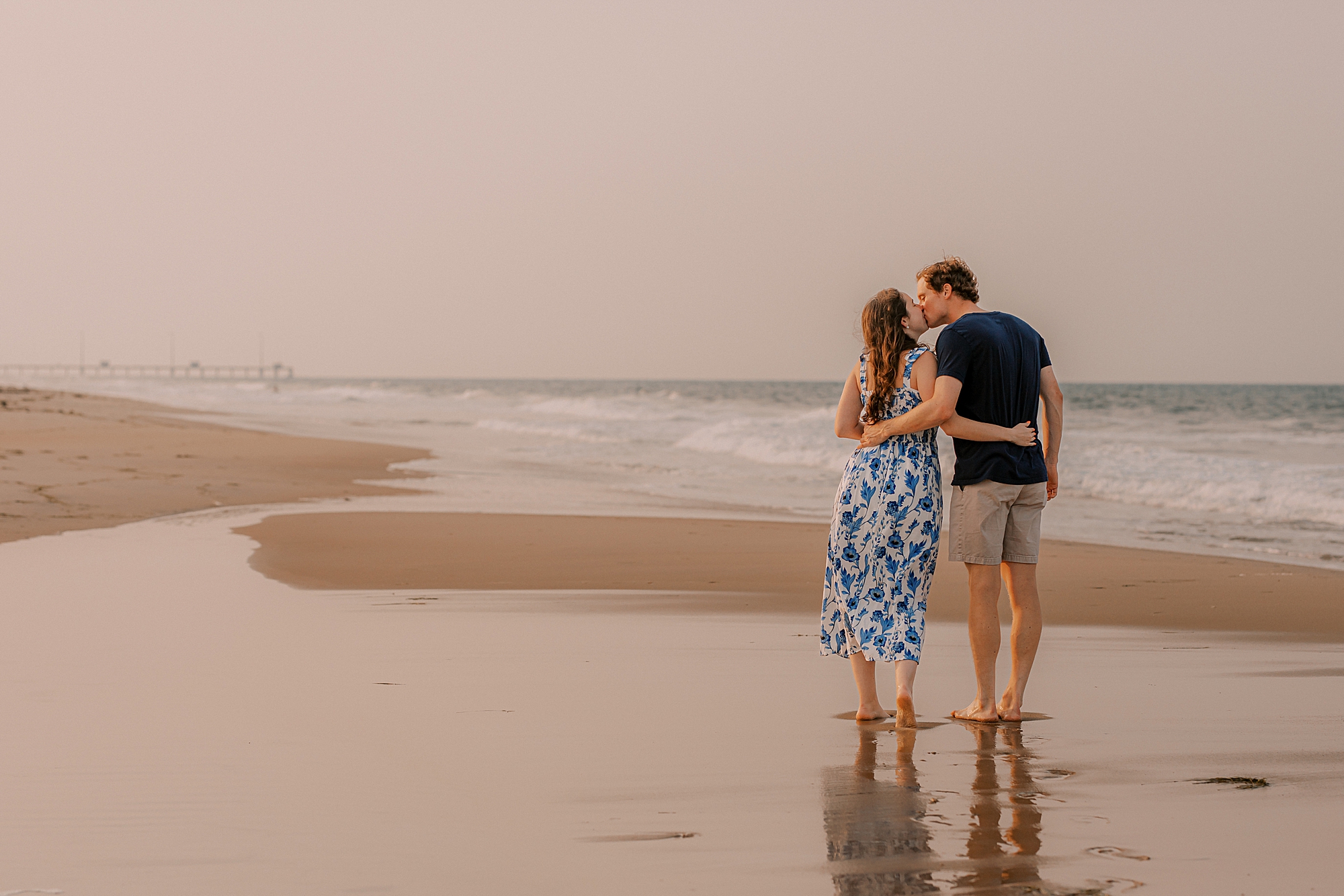 man hugs woman around waist leaning to kiss her standing hip to hip in surf 