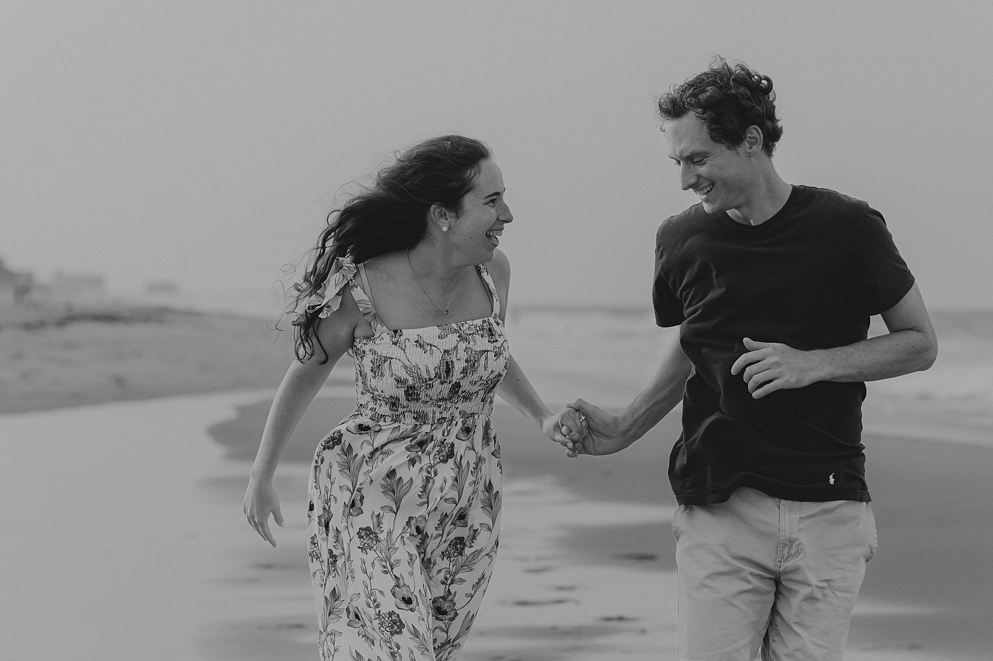 engaged couple holds hands running through water on beach in the outer banks