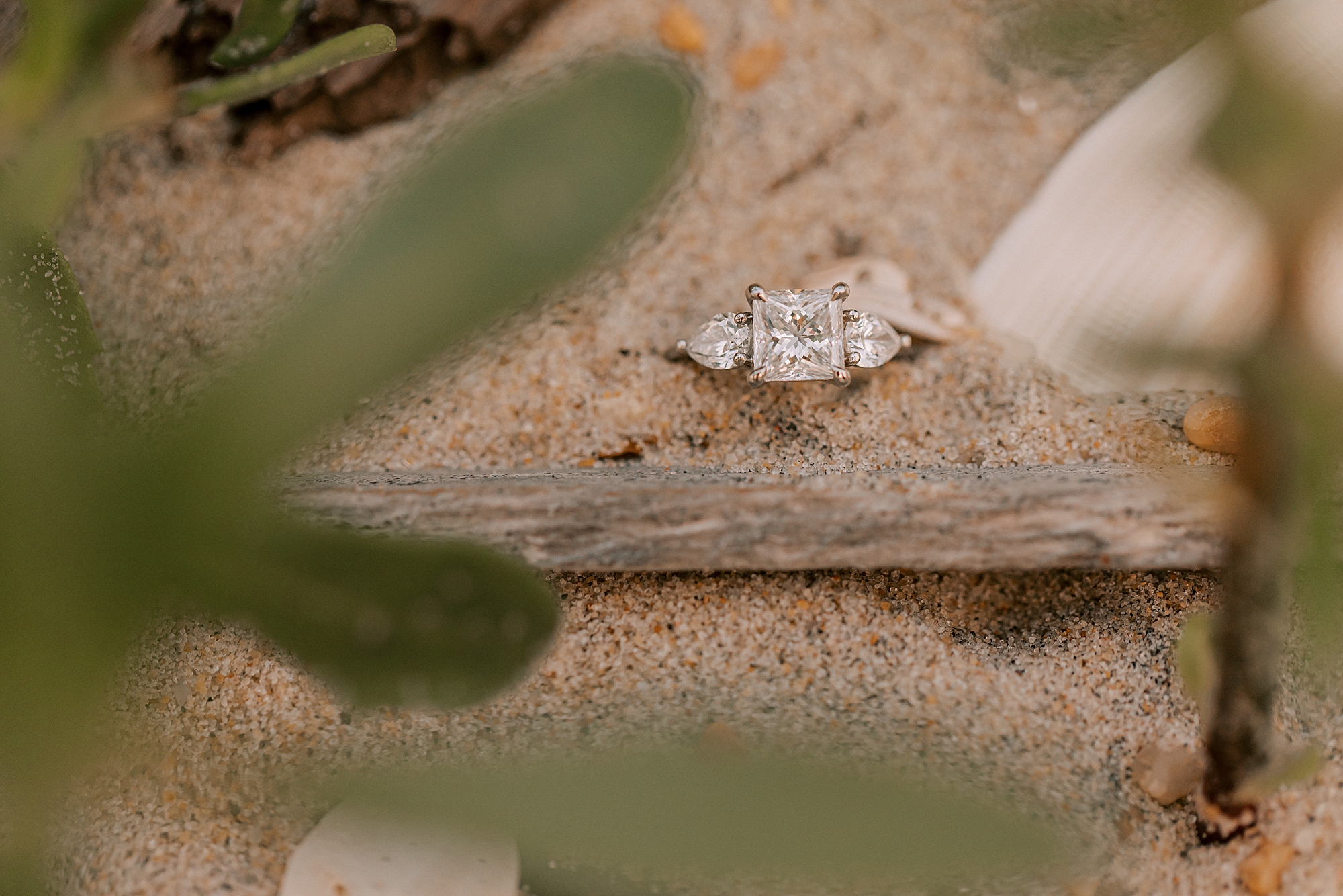 diamond ring rests in sand by driftwood on outer banks beach