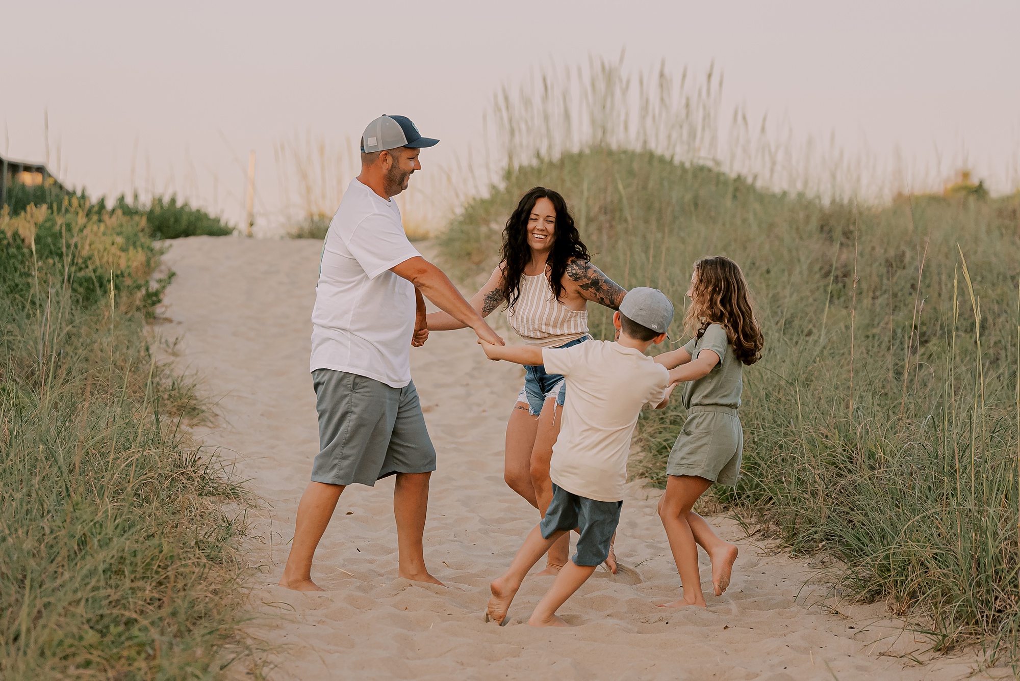 parents twirl around on beach dune with two children during family photos in nags head nc