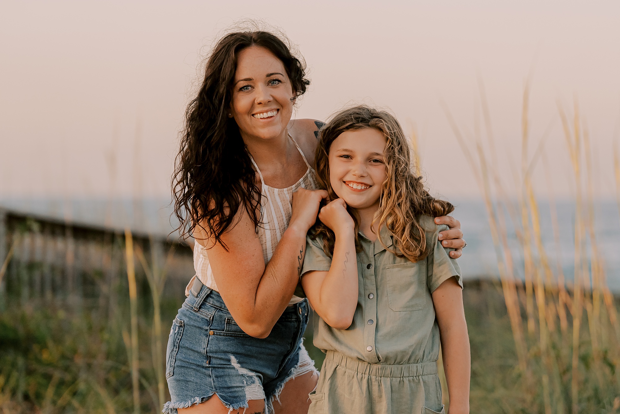 mom and daughter hug between tall beach grass on sand dunes 