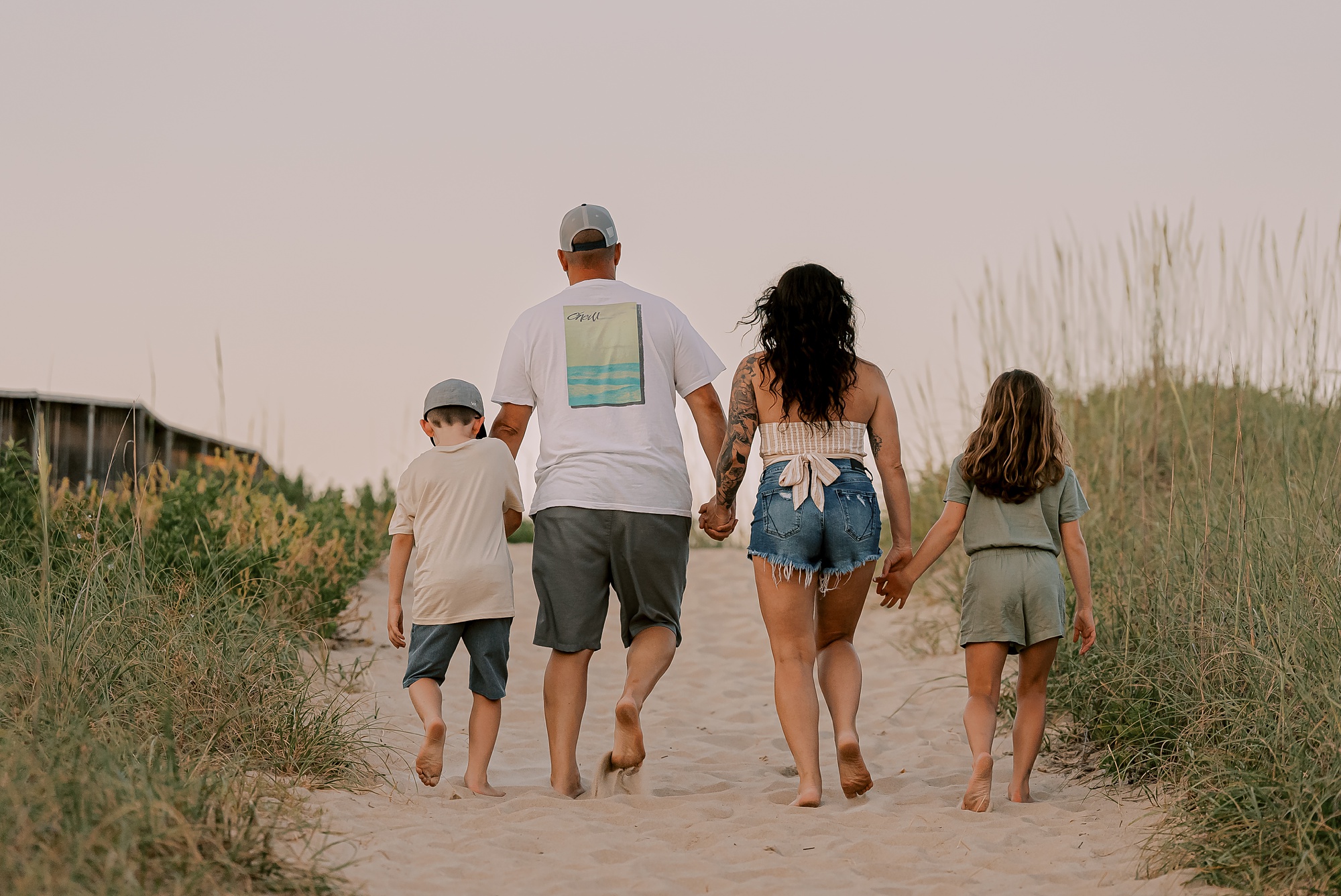 family of four holds hands walking up sand dune during photos with outer banks family photographer