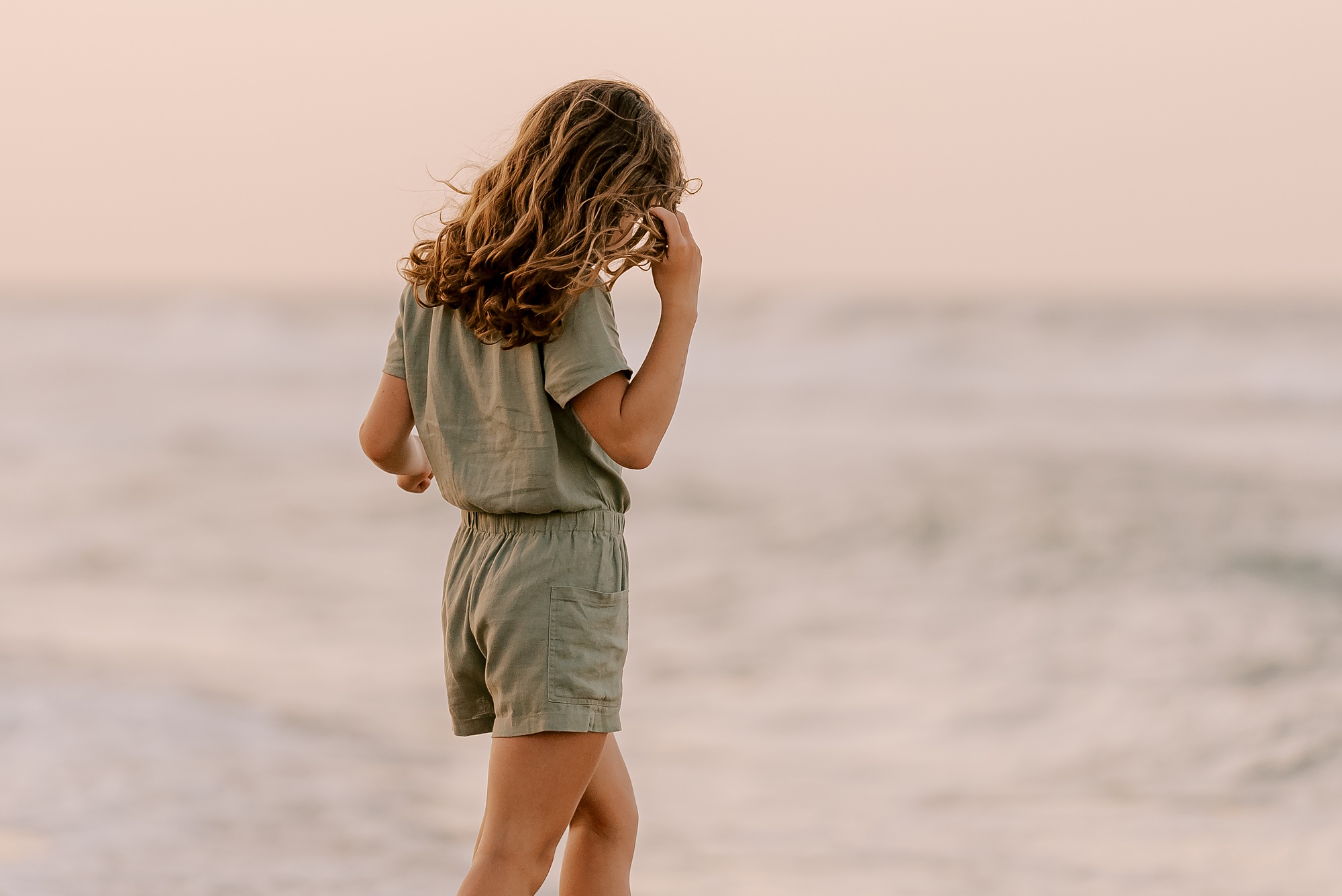 girl in olive green jumpsuit walks through water on beach in NC