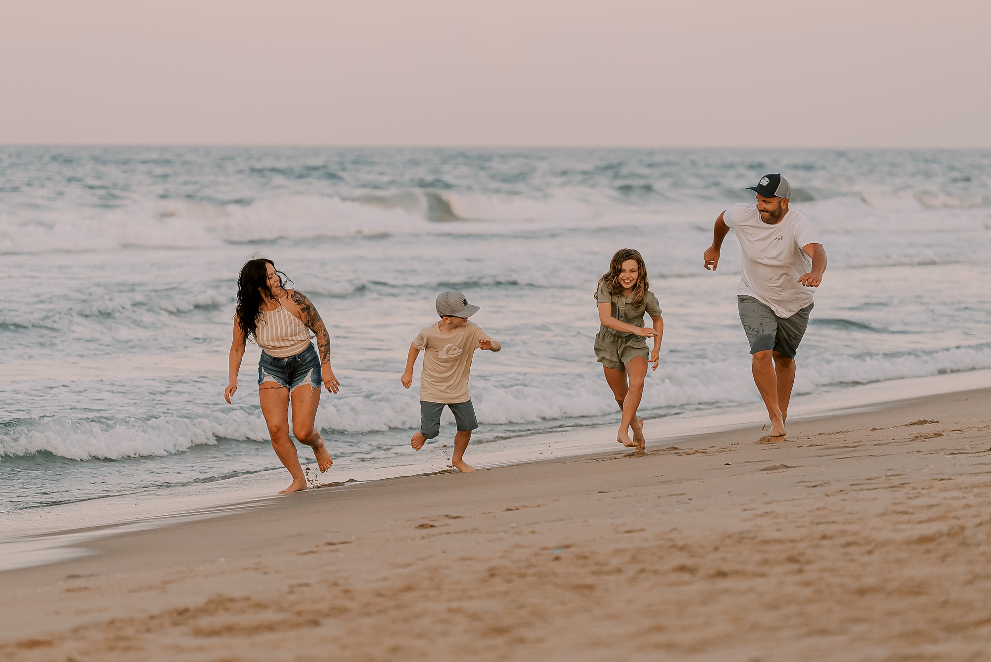 family of four runs along the beach during photos with outer banks family photographer