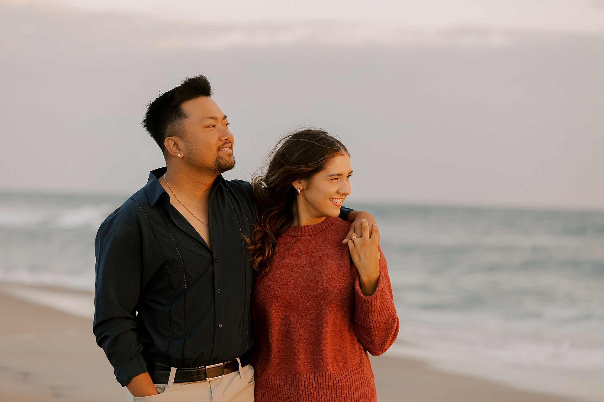 man stands with arm around woman's shoulder during sunset photos on the beach