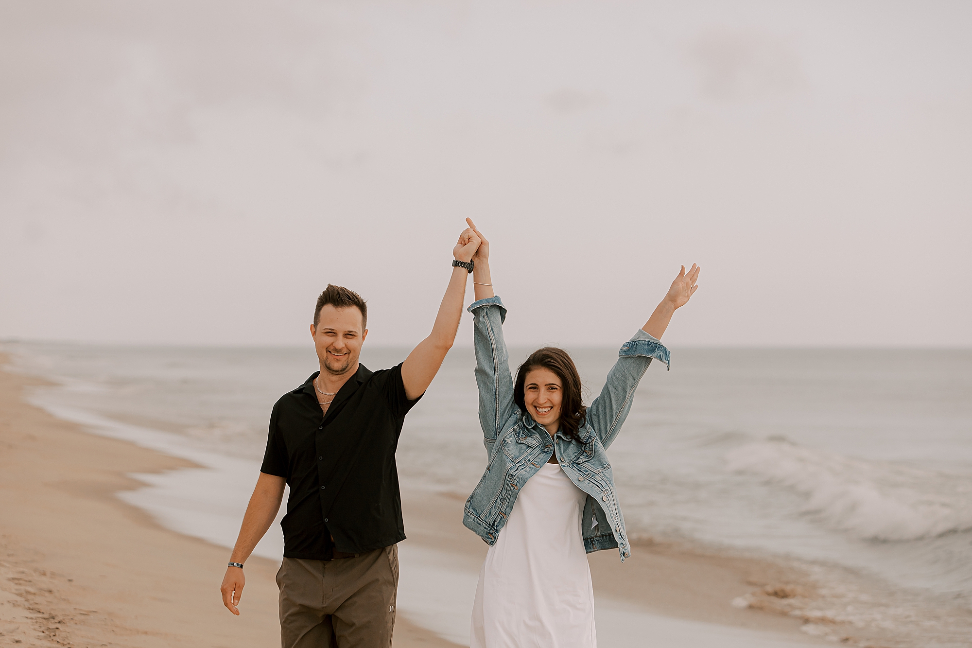 couple cheers holding hands on the beach in kitty hawk nc