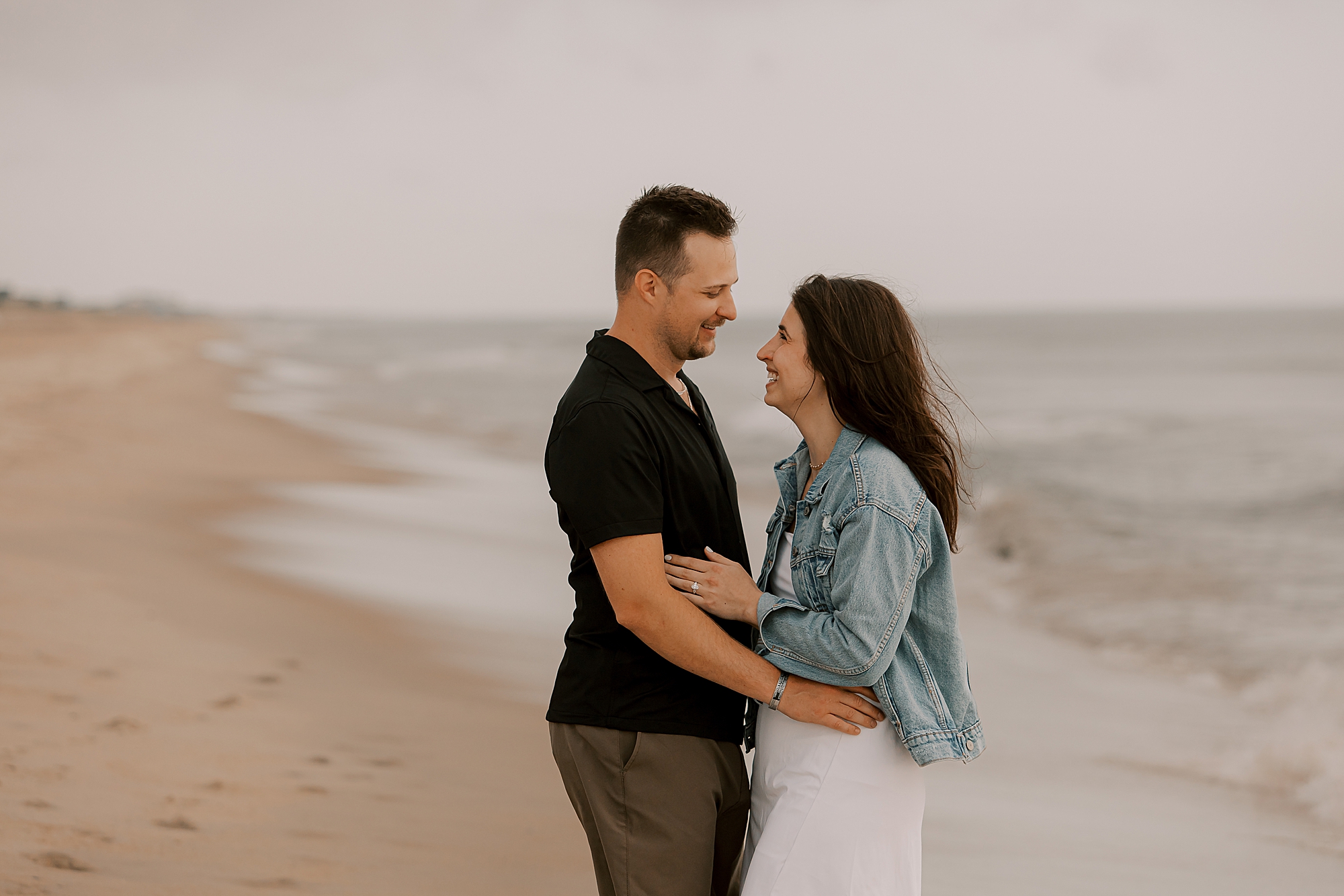 man and woman hug standing by ocean at kitty hawk beach